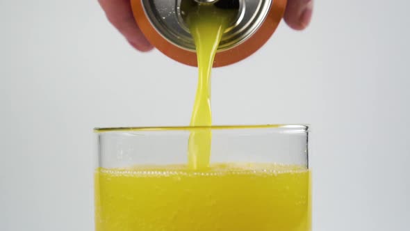 Citrus carbonated drink with bubbles is poured into a glass from an aluminum can in a hand