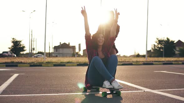 Cheerful Woman Sitting on a Longboard and Raising Her Hands Up Happily While Her Friend is Pushing