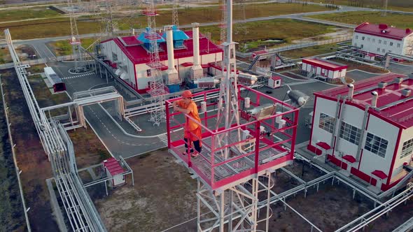 The Drone Flies in a Circle Around a Metal Tower of Illumination on Which a Worker in Orange Clothes