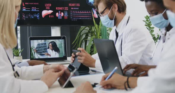 Medics in Masks Sitting at the Joint Workplace and Watching Video Conference