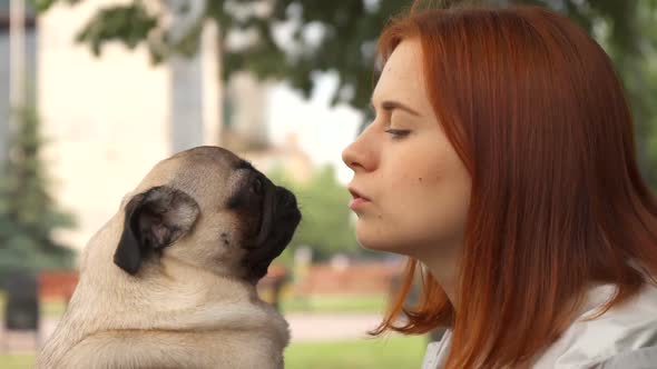 Girl Trying To Kiss Her Pug and Looking at Camera