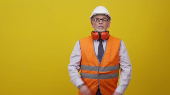 Adult engineer man in a working uniform folds arms cross on chest, in an orange background studio.