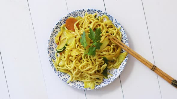 Traditional Noodles with Chicken and Vegetables Served on Ceramic Plate with Chopsticks on Side