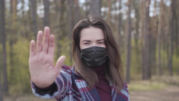 Young Caucasian Woman in Face Mask Showing Stop Gesture at Camera. Portrait of Confident Brunette