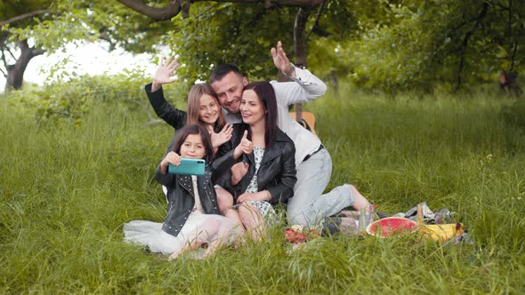 Cheerful Parents and Their Cute Daughters Sitting Together on Green Grass and