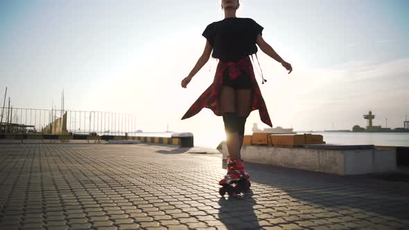 Young Stylish Funky Girl with Green Hair Riding Roller Skates on Sea Port Background During Sunset