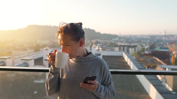 Woman Starts Her Day with a Cup of Tea or Coffee and Checking Emails in Her Smartphone on the