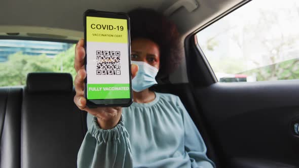 African american businesswoman with face mask preparing covid 19 certification on smartphone