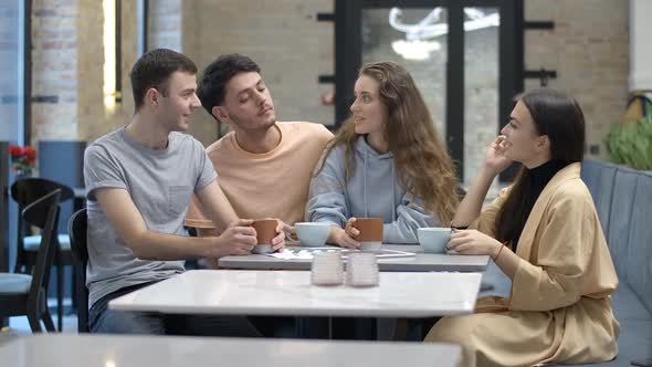 Four Young Caucasian Men and Women Talking Sitting in Cafe Turning To Camera and Smiling