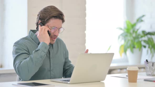 Angry Man with Laptop Talking on Smartphone