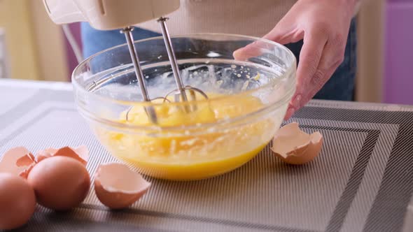 Female Hands Stirring Dough with a Mixer for Cake in a Bowl on a Table