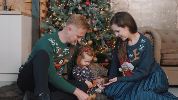 Young Couple Playing with Their Little Daughter Near Christmas Tree at Home