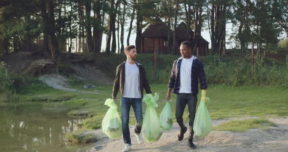 Young Men Carrying Plastic Bags Near the Lake After Cleanup Surrounding Territory from Rubbish