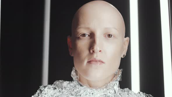 Bald Woman in Foil Wear Looking at Camera in Dark Studio with Flickering Light