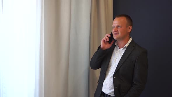 A Businessman in a Jacket Talking on the Phone in a Hotel Room