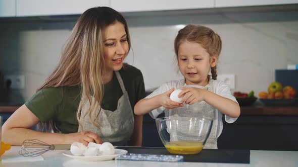 Woman Looks at Little Girl Cracking Chicken Egg Into Bowl