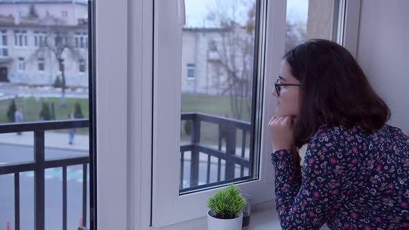 A Brunette Girl in Glasses Stands at the Window in Anticipation Side View Copy Space