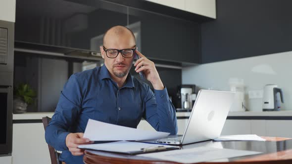 Man Talking on Phone and Checking Papers in Home Office