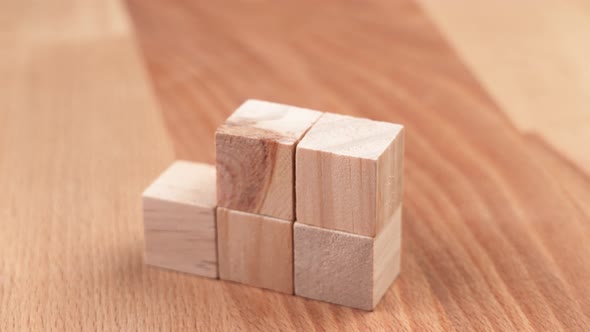 A hand placing a green toy cube on top of a tower of wooden blocks