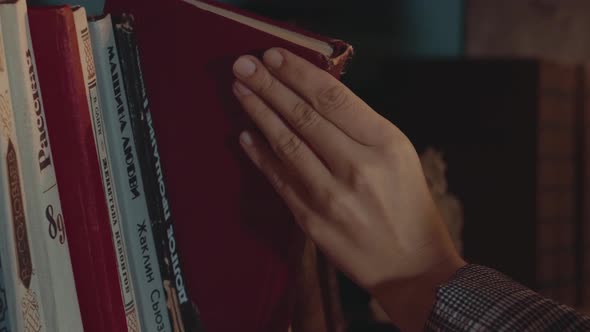 Young Attractive Caucasian Woman Runs Her Hand Through the Books on the Shelf Before Choosing One