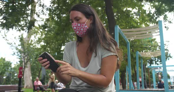 Woman Wearing Mask in Park Using Mobile Phone