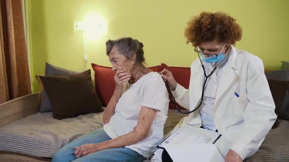 Mature Woman Doctor Holding Stethoscope Examining Senior Grandma Patient at Home