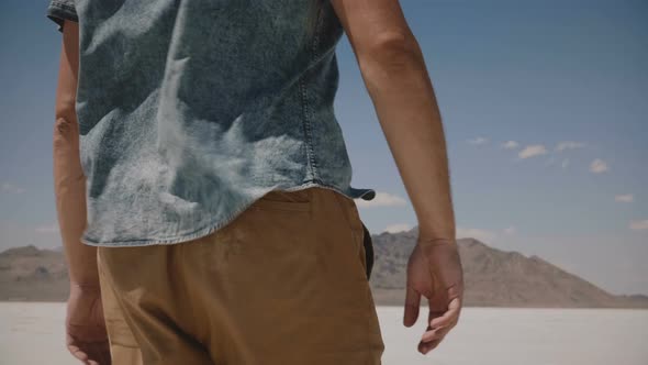 Close-up Camera Follows Free Man in Casual Clothes Walking Along, Looking Around Windy Salt Lake