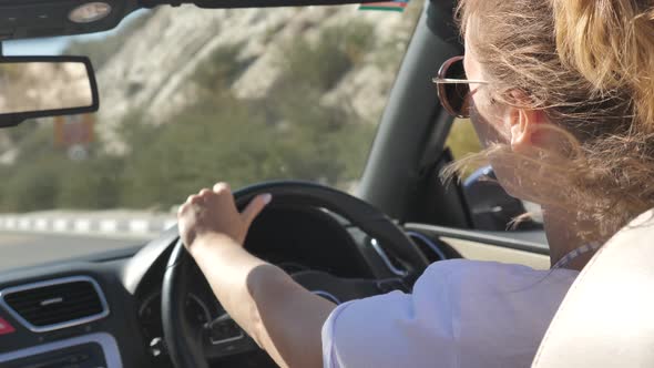 Young Woman Driving Cabriolet Car by Country Road Inside Back View