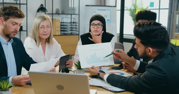 Businessman Sitting at Workplace Together with Another Members of Workteam and Explaining Results