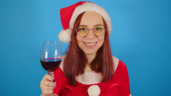 Woman in santa costume with glass of red wine on blue background.