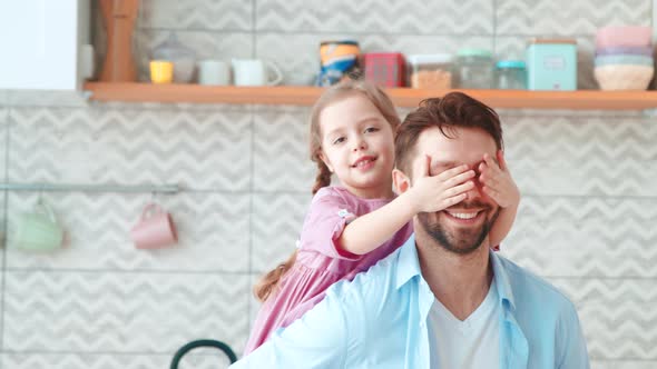 A little preschool girl covers her dad's eyes with her hands