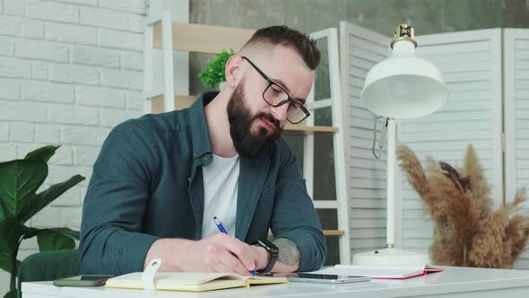 Bearded Man Learn Online Courses Using a Tablet and Write Notice in His Notebook