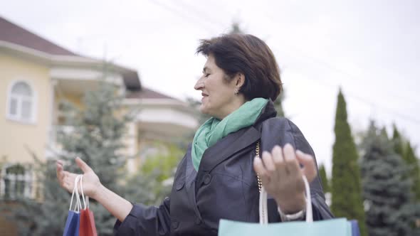 Happy Female Shopper Standing Outdoors Raising Hands with Shopping Bags and Smiling