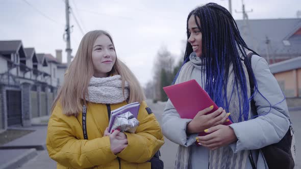 Smiling Female Teen Friends Walking Along the Street and Talking. African American and Caucasian