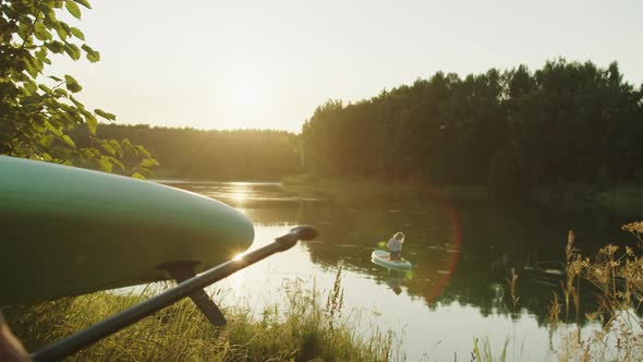 Woman Swimming Sitting on Surfing Board in Sunlight While Man Surfer Going to River with Surfboard