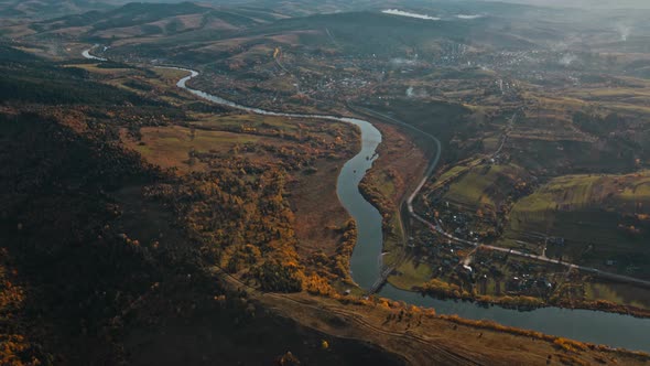 Aerial Drone View Flight Over Autumn Countryside Village Along Curving River and Road in Mountain