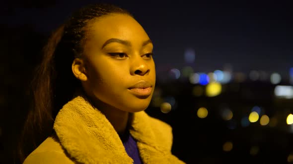 A Young Black Woman Looks Seriously at the Camera in an Urban Area at Night  Side Closeup