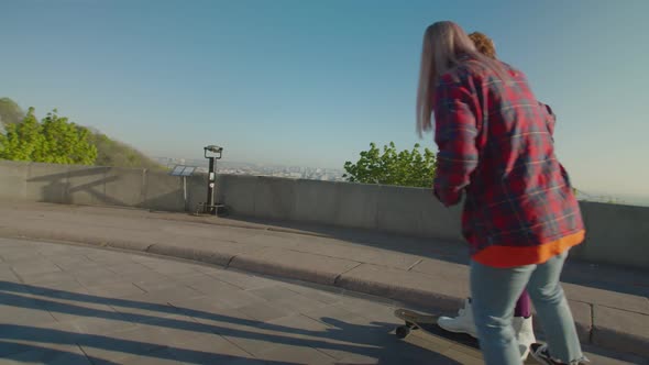 Pretty Black Female Skateboarding with Support From Friend in City at Daybreak