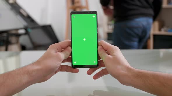 Mans Point of View Holding a Smartphone Vertically with Green Screen on