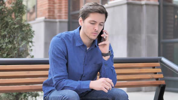 Young Man Talking on Phone Sitting Outdoor on Bench