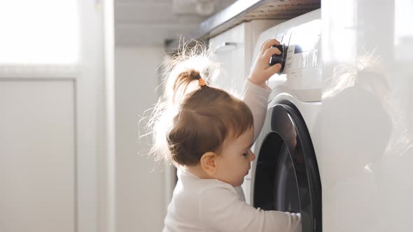 Side View Cute Baby Daughter Playing at Washing Machine in Kitchen of Comfortable Home