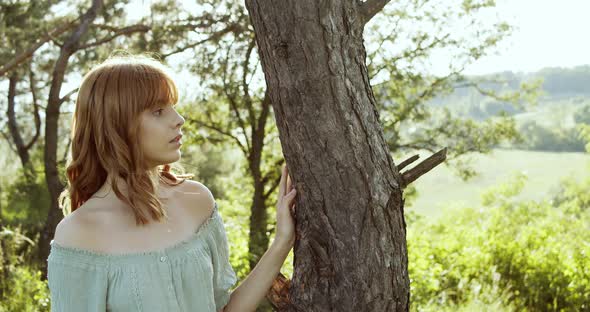 Attractive European Chestnut Teen Girl with Natural Makeup Has a Pleasure of Nature Near a Tree in