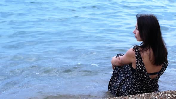 A beautiful sexy young girl sits on the shore of the ocean and looks into the distance.