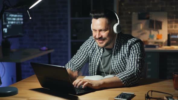 Happy Office Worker in Headphones Listening To Music Busy with Laptop at Night