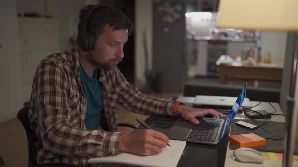 A Male American Student Studies Online at Home in a Studio Apartment Sitting at His Desk with His