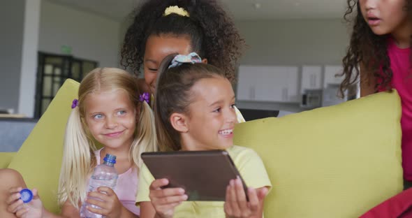 Video of diverse girls sitting at school common room with tablet, talking and laughing