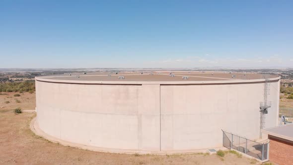 DRONE Reveal Shot of Water Supply Tank supplying water to a Town in the Background on a Sunny Day