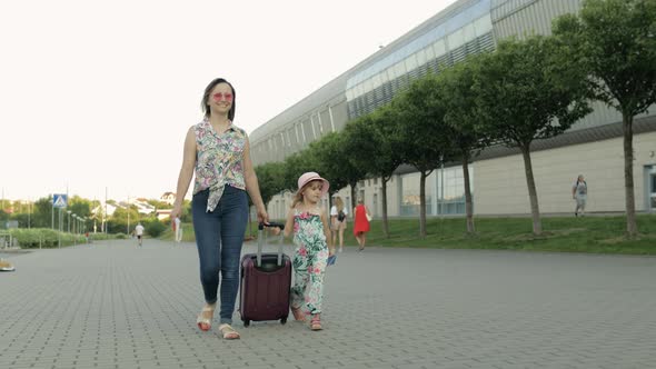 Mother and Daughter Walking Outdoors To Airport. Woman Carrying Suitcase Bag. Child and Mom Vacation