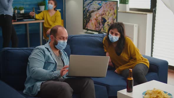 Man with Mask Showing New Movie on Laptop to Woman