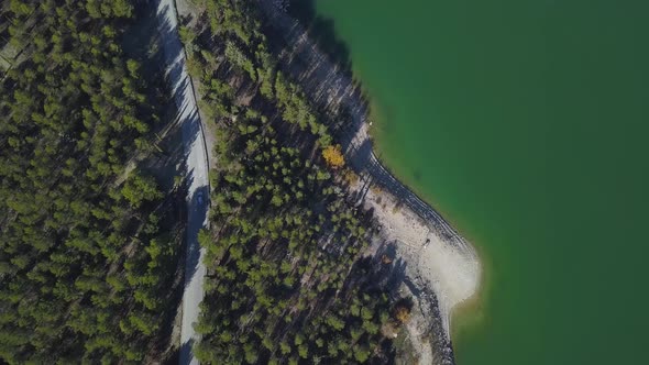 Camera following a car driving through a road in the forest close to a lake. Overhead view.